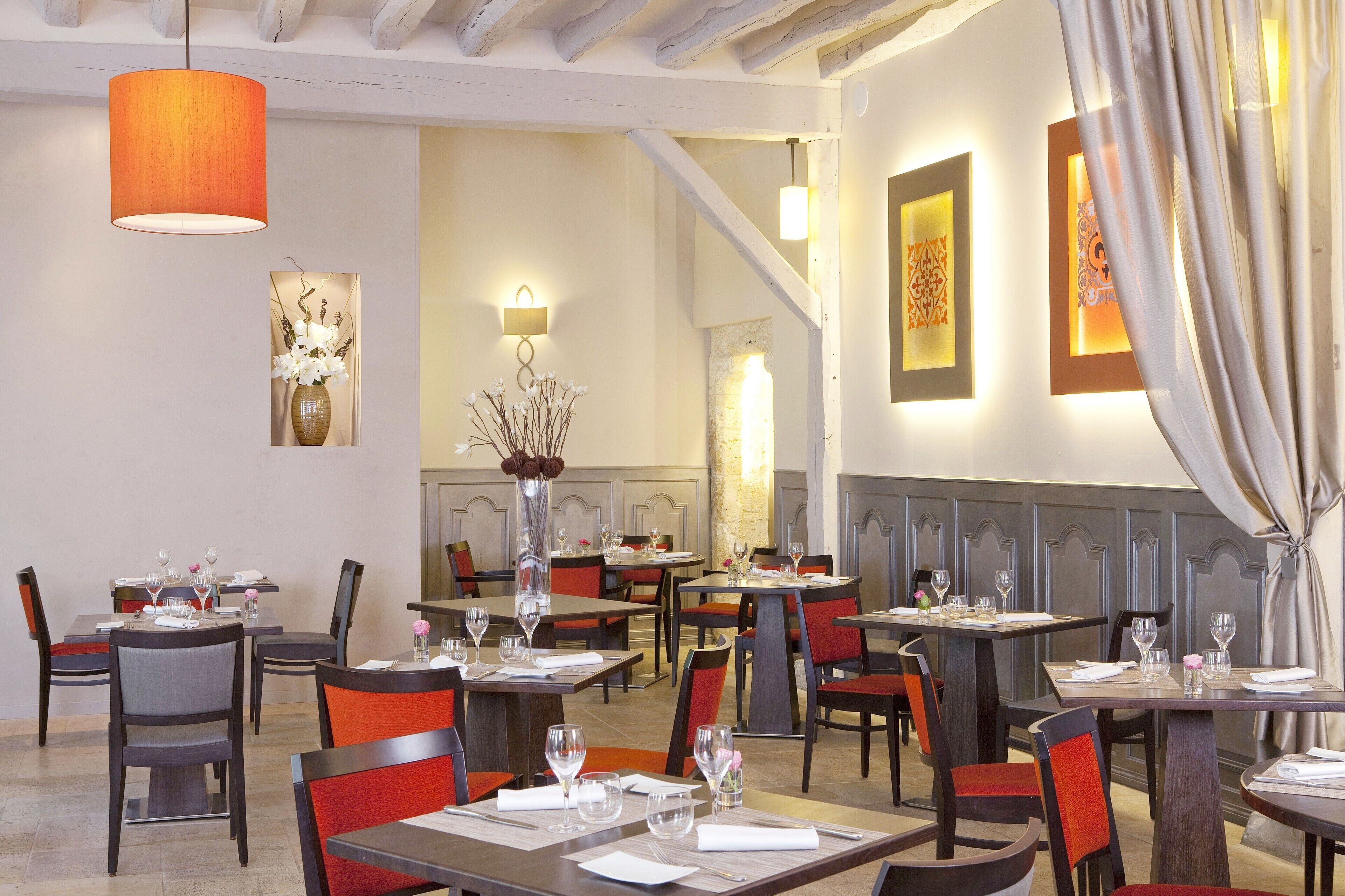 Un restaurante con varias mesas y sillas, una lámpara colgante color naranja y obras de arte enmarcadas en las paredes.