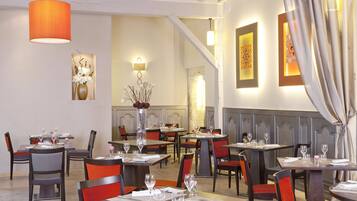 Un restaurante con varias mesas y sillas, una lámpara colgante color naranja y obras de arte enmarcadas en las paredes.