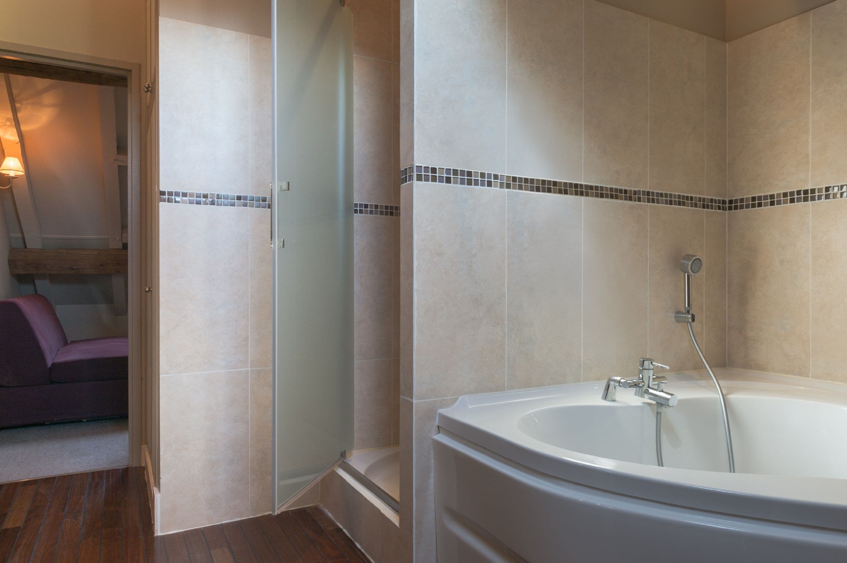 A bathroom with a bathtub, shower, and a glass door leading to a seating area.
