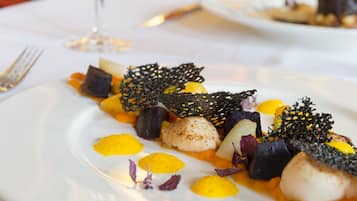 A white plate with a seafood dish, including scallops and vegetables, on a white tablecloth.