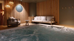 Un cuarto de spa con un jacuzzi, un sofá, una silla y paneles de madera.