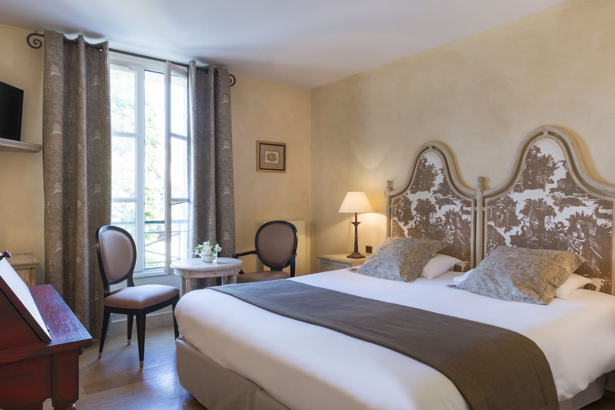 A hotel room with a bed, two chairs, a desk, and a window with curtains.