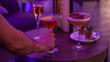 A table with three drinks, a menu, and a person sitting on a couch.