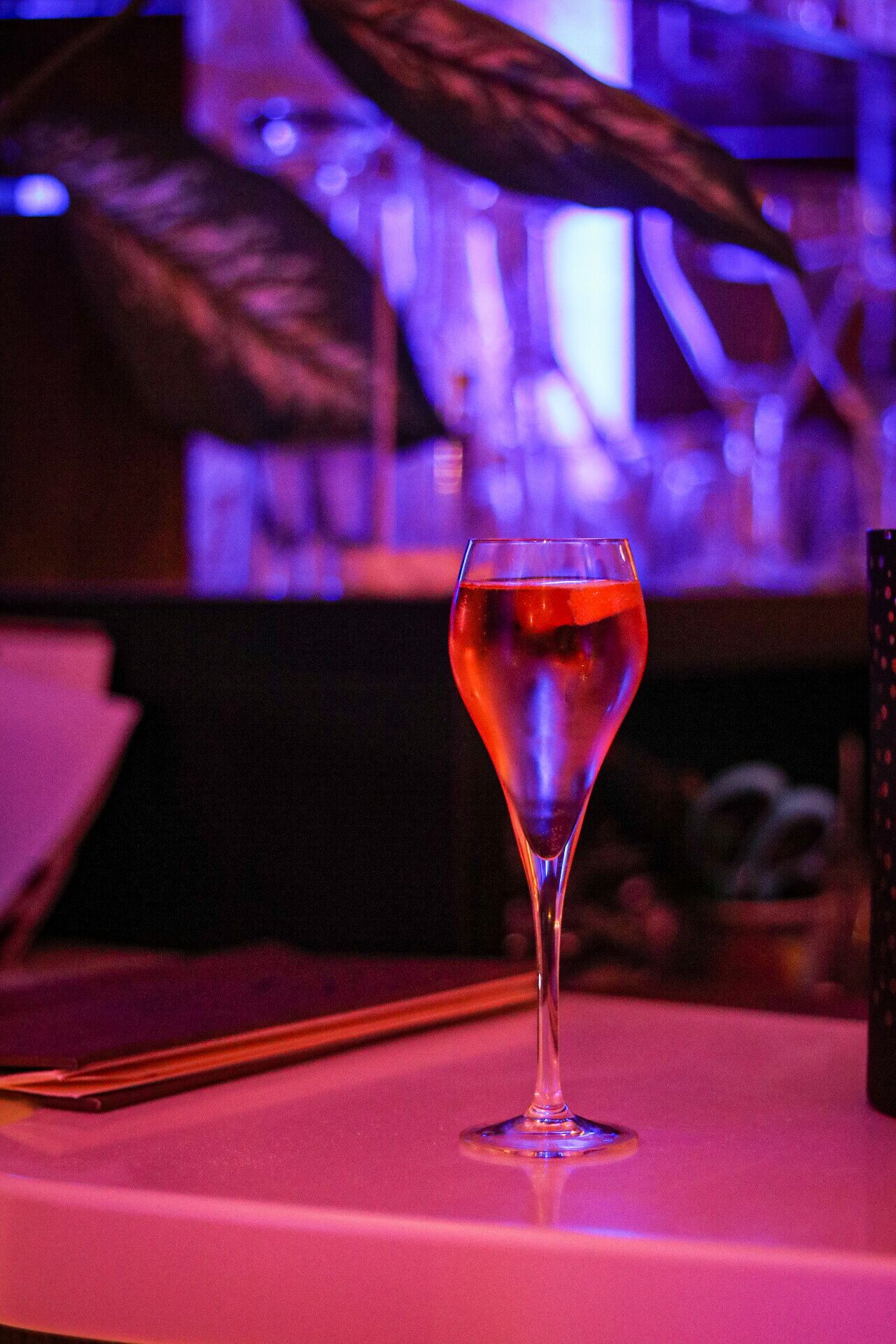 A glass of red beverage on a table in a dimly lit setting.