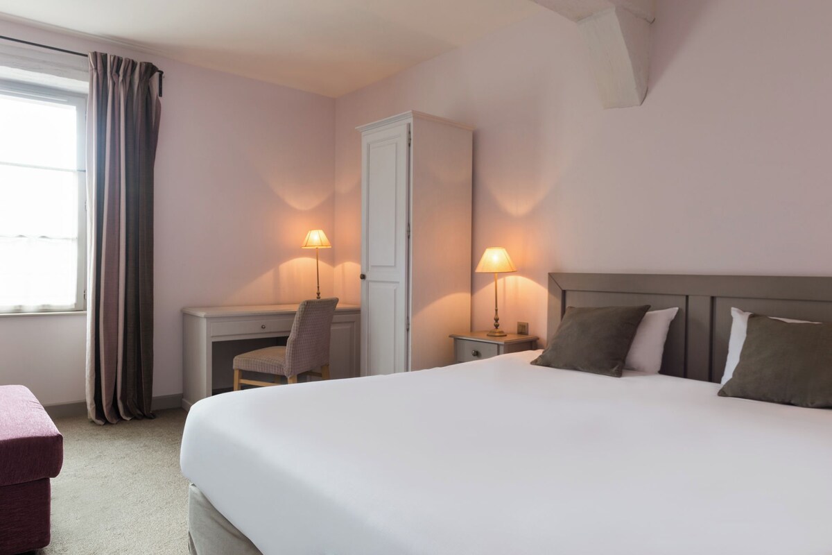 A hotel room with a large bed, a desk, a chair, and two bedside lamps.