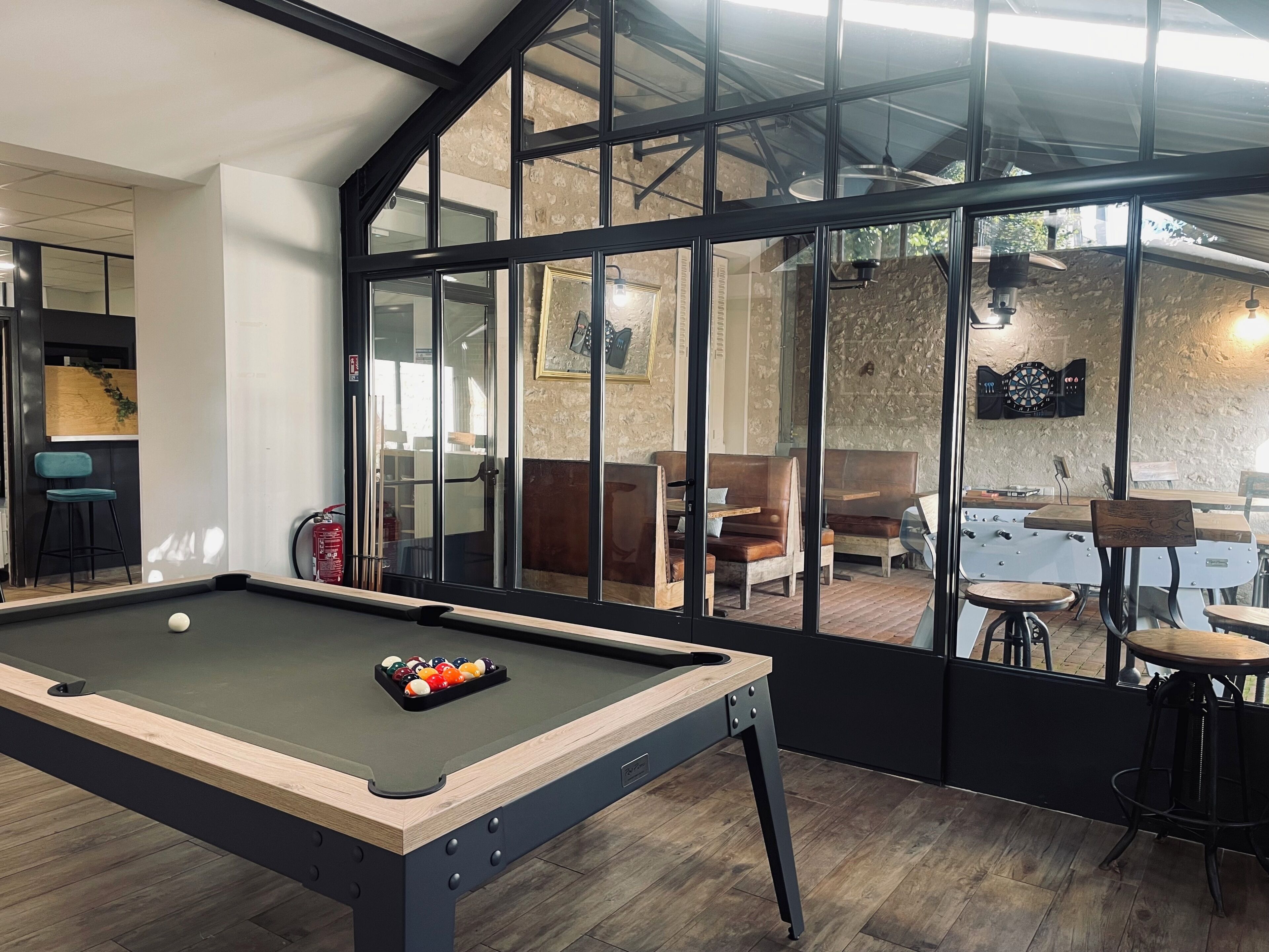 Una mesa de billar con bolas, un dardo y una mesa de billar en una sala con ventanas grandes y pared de piedra.