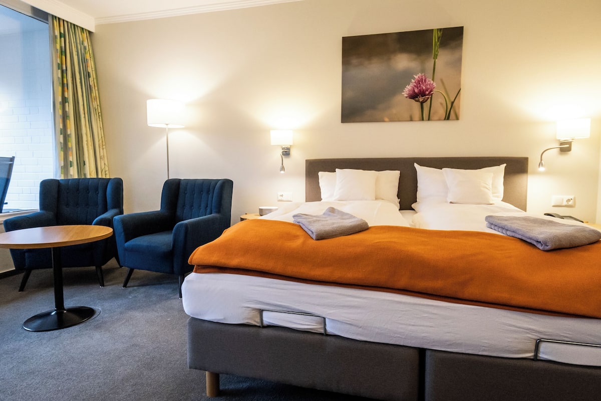 A hotel room with a large bed, two armchairs, a small round table, and a painting on the wall.