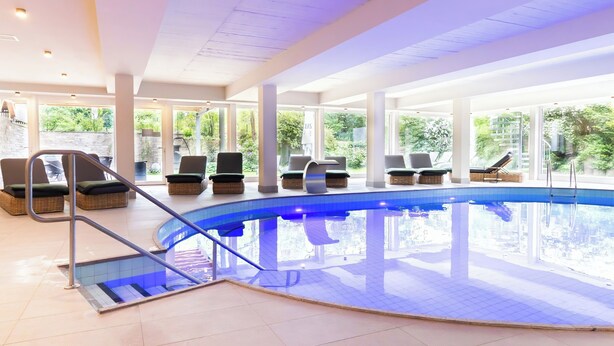 An indoor swimming pool with lounge chairs and a glass balustrade. - VitalHotel Ascona (Bad Bevensen)