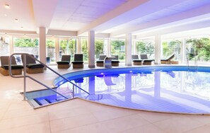 An indoor swimming pool with lounge chairs and a glass balustrade. - VitalHotel Ascona (Bad Bevensen)
