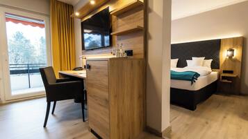Een hotelkamer met een bed, een bureau, een stoel, een aan de muur bevestigde televisie en een raam met gordijnen.