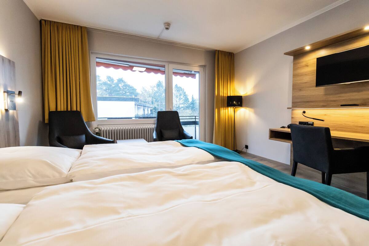 A hotel room with two beds, a desk, a chair, a TV, and a window with curtains.