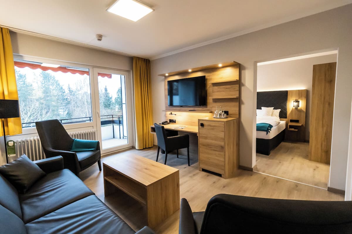A modern hotel room with a sofa, a desk, a television, and a bed.