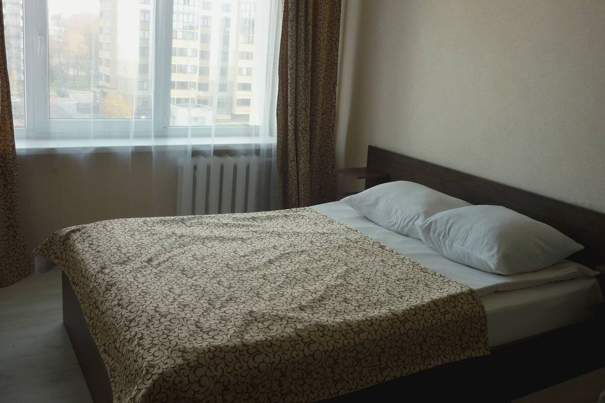 Un dormitorio con cama, ventana con cortinas y radiador.