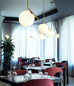 A modern dining area with tables set for service, a potted plant, and a large window with curtains. - Il Palazzin Hotel (St. Paul's Bay)