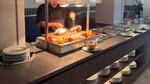 Montaje de bufé con un chef preparando comida, una variedad de platos y platos apilados ordenadamente.