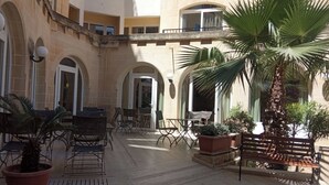 Un patio con mesas al aire libre, palmeras y un edificio de piedra con arcos.