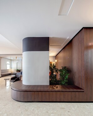 A modern lobby with a curved reception desk, seating area, and a large plant. - Il Palazzin Hotel (St. Paul's Bay)