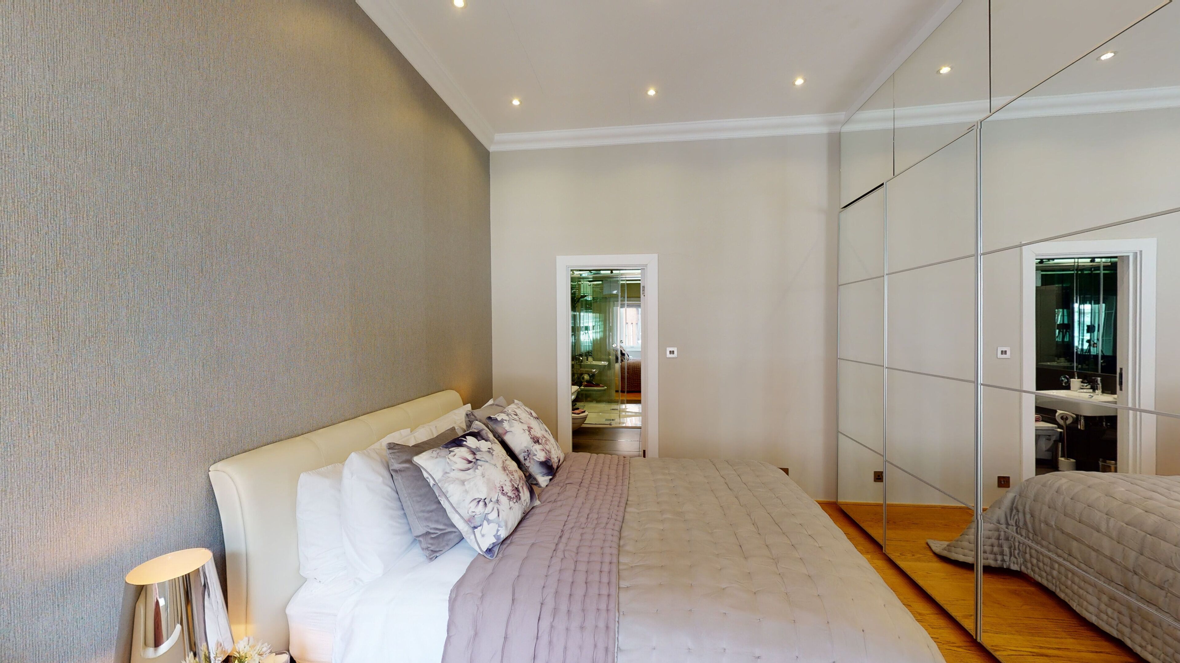 Une chambre moderne avec un grand lit, une lampe de chevet et une armoire avec un miroir.