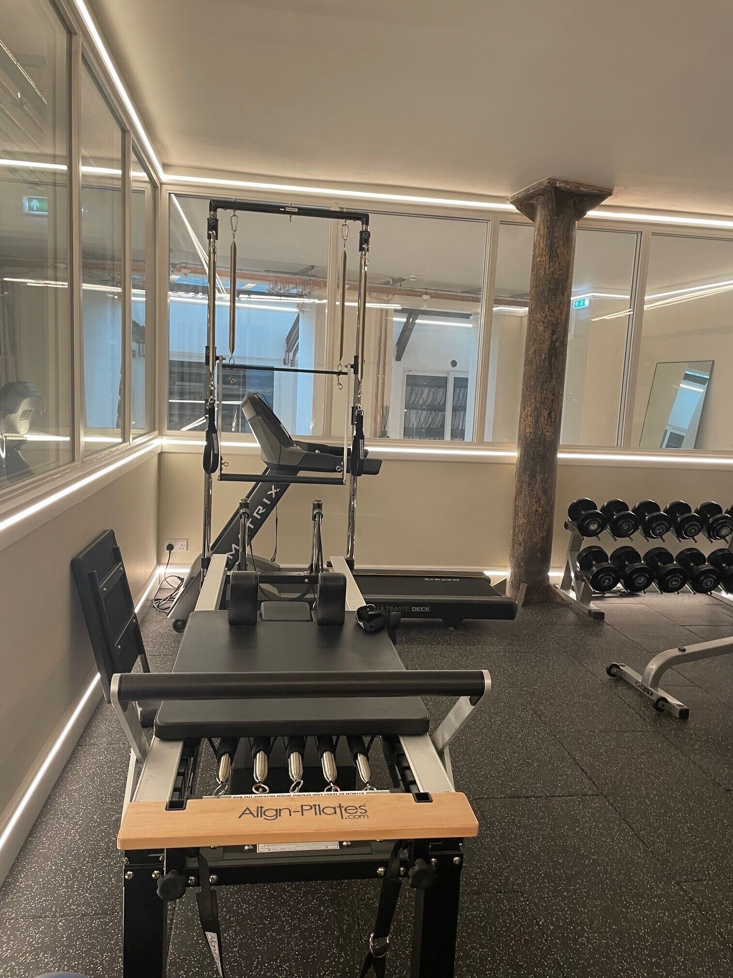 A gym with a Pilates reformer machine, weight racks, and a bench.