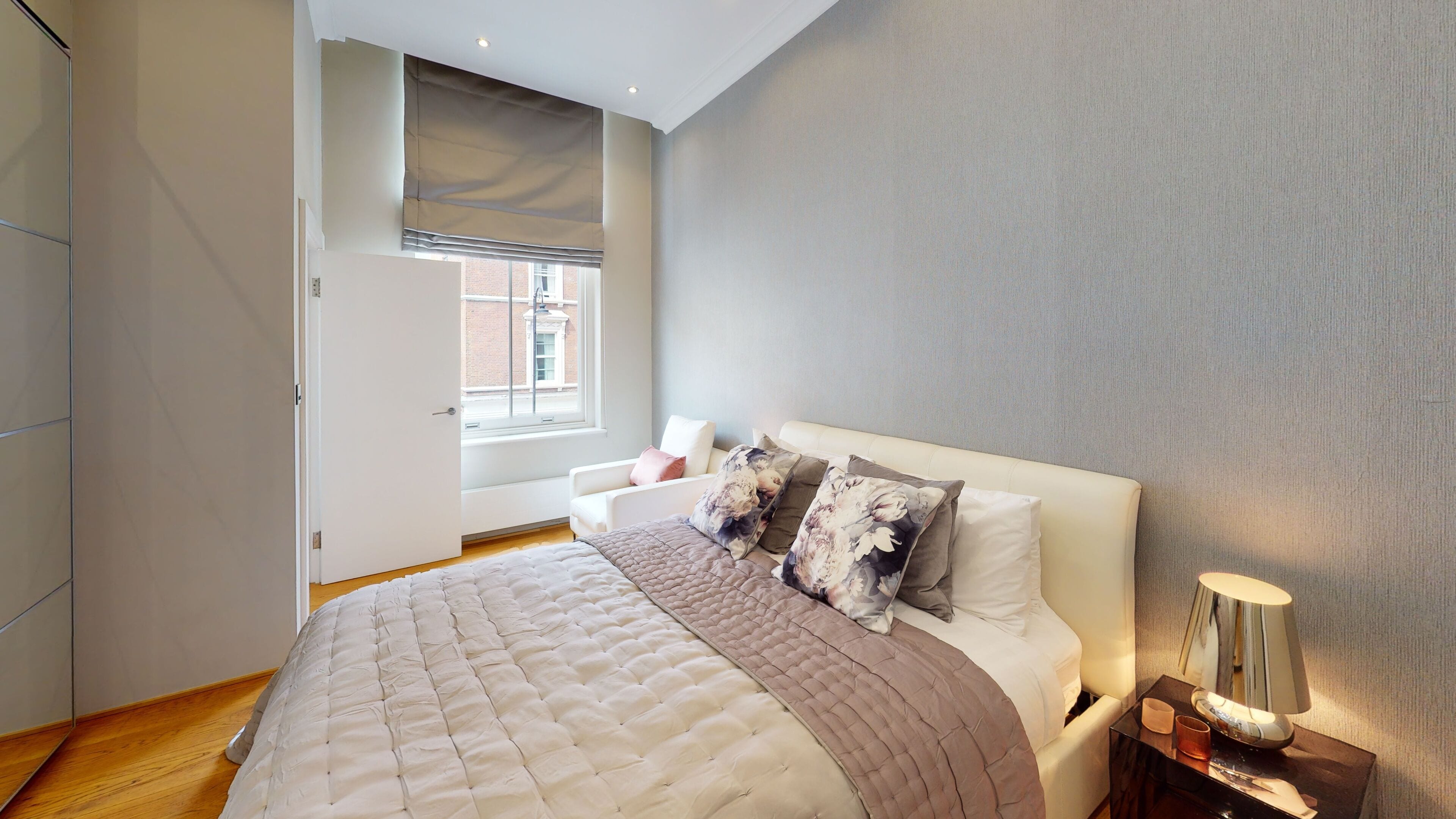 A bedroom with a large bed, a window, a chair, and a bedside table with a lamp.