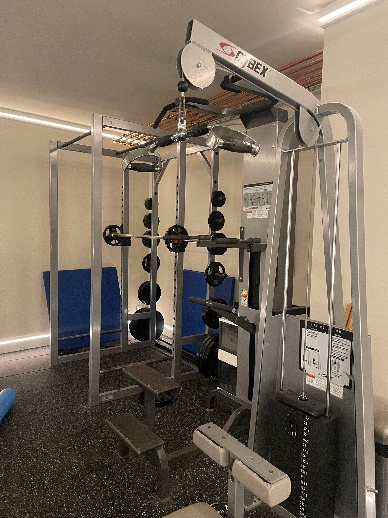 A gym with a squat rack, weight plates, and a bench.
