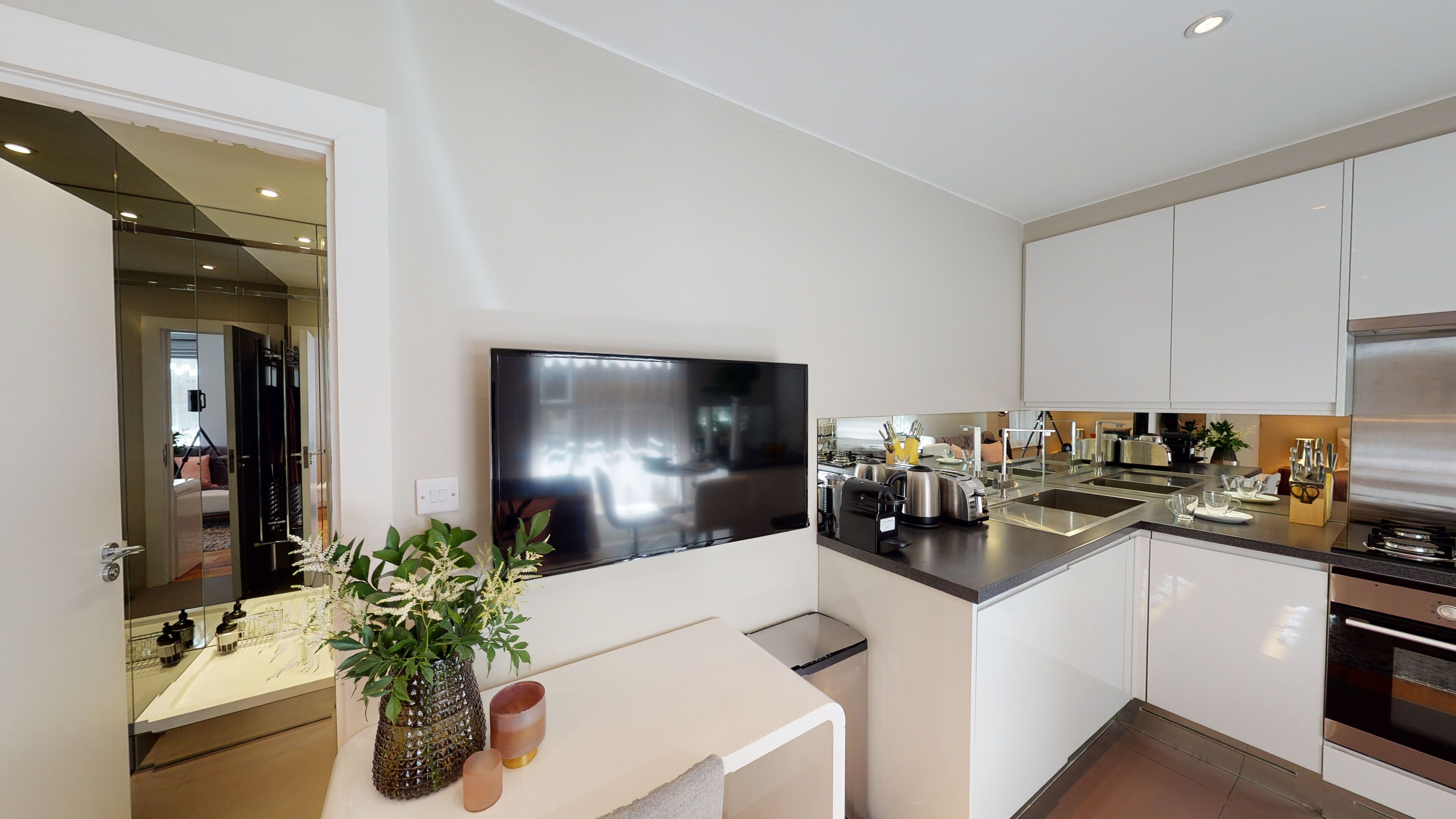 A modern kitchen with a flat-screen TV, stainless steel appliances, and a minimalist design.