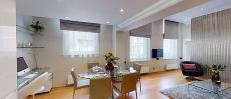 Een moderne woonkamer met een glazen eettafel, comfortabele zithoek, een flatscreen televisie en een knusse open haard.