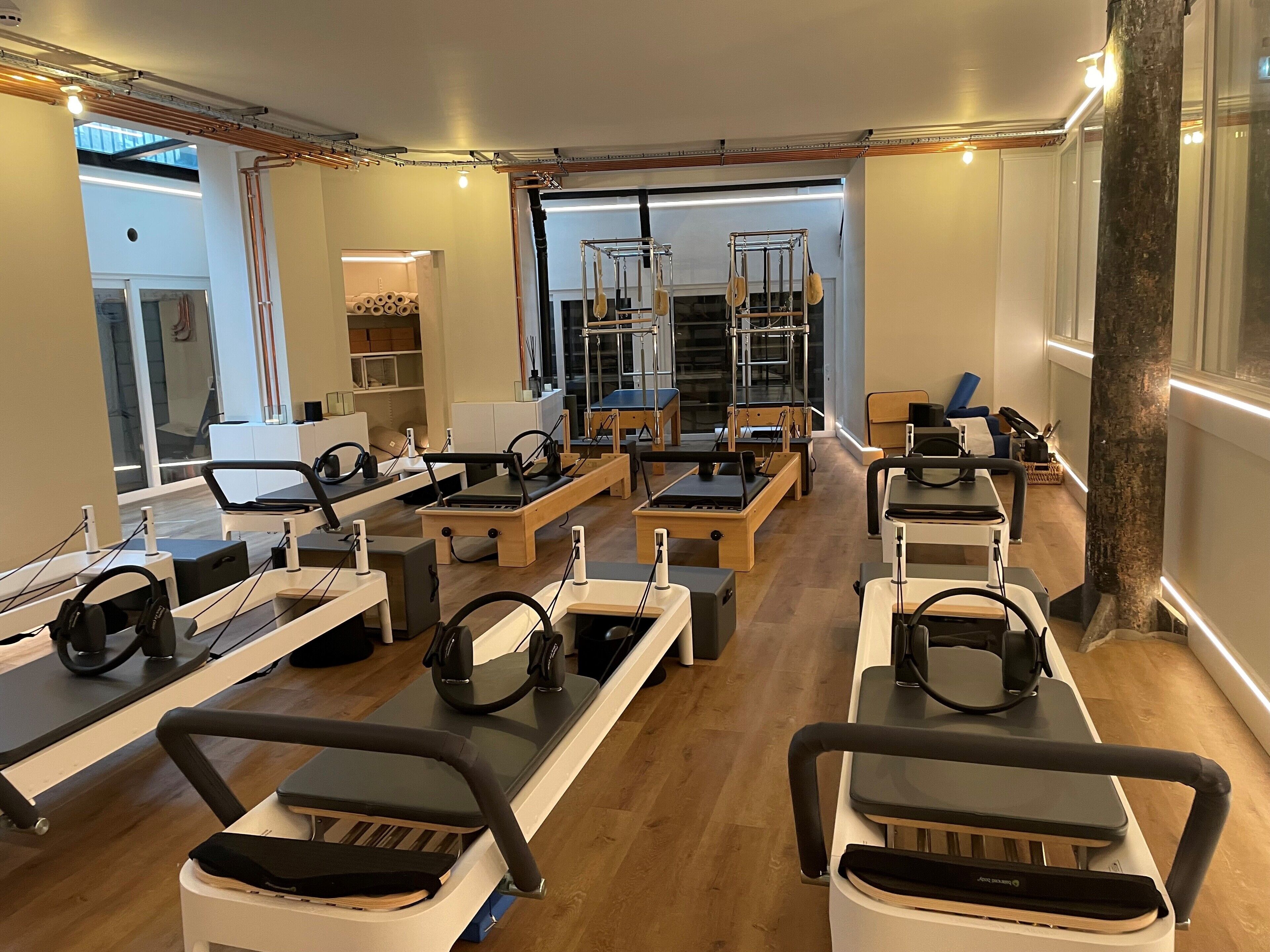 A Pilates studio with equipment arranged in rows, large windows, and a visible door leading outside.