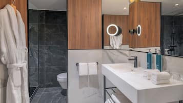 A modern bathroom with a wooden vanity, a large mirror with lights, a toilet, and a shower area.