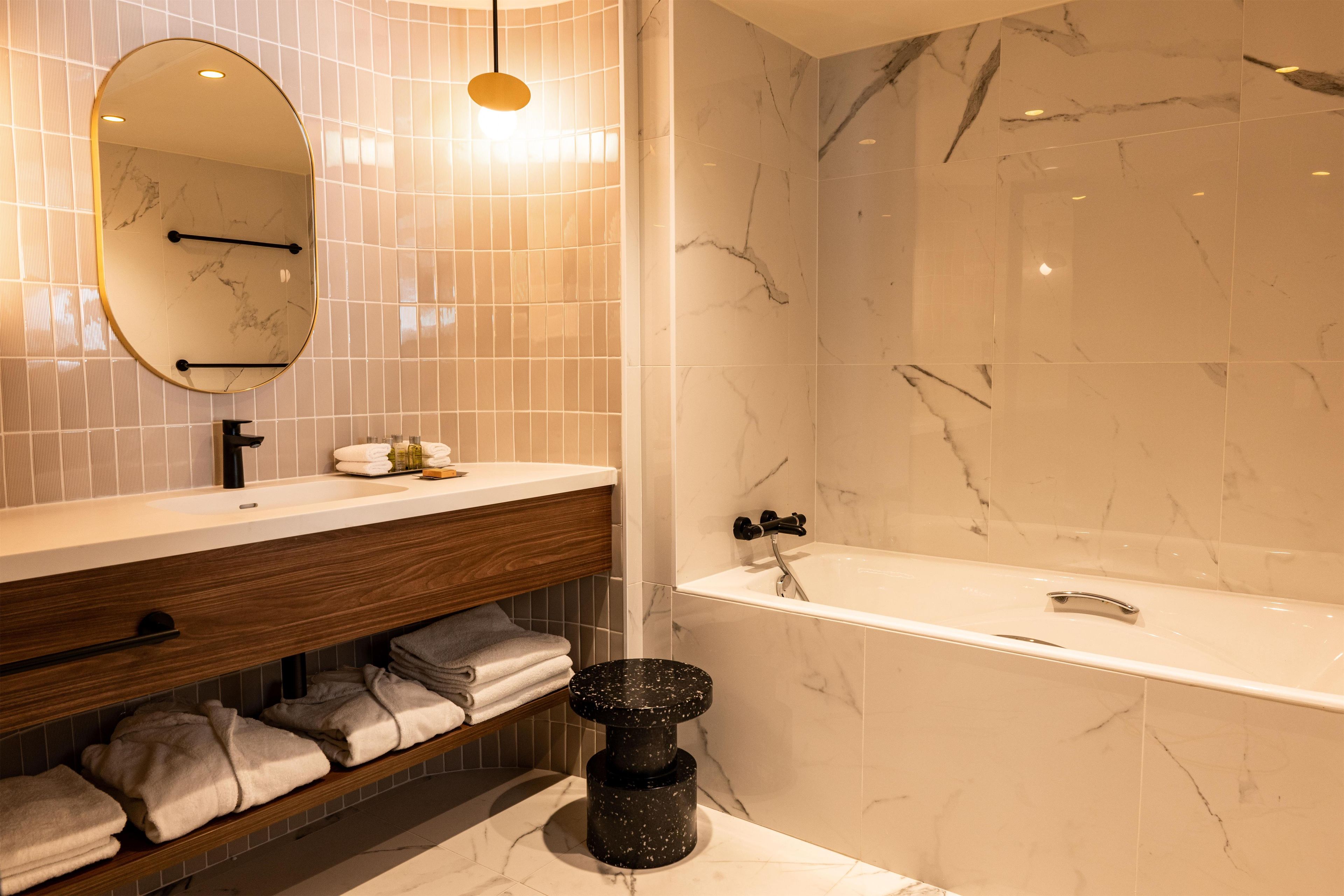 A modern bathroom with a marble sink, a wooden vanity, a large mirror, and a bathtub.