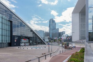 Un hotel moderno con fachada de vidrio, un llamativo letrero de Hilton y una plaza con una estructura arquitectónica singular al fondo.