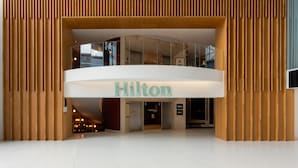 L'ingresso moderno di un hotel con un grande cartello 'Hilton', una facciata in vetro e un pavimento piastrellato pulito.