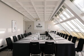 A conference room with a long table, black chairs, and a 'Hilton' sign on the wall. - Hilton Paris La Defense Hotel (Puteaux)