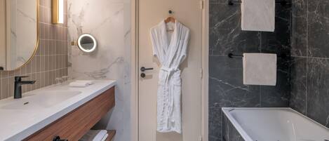 A modern bathroom with a marble vanity, a bathtub, and a robe hanging on the door.