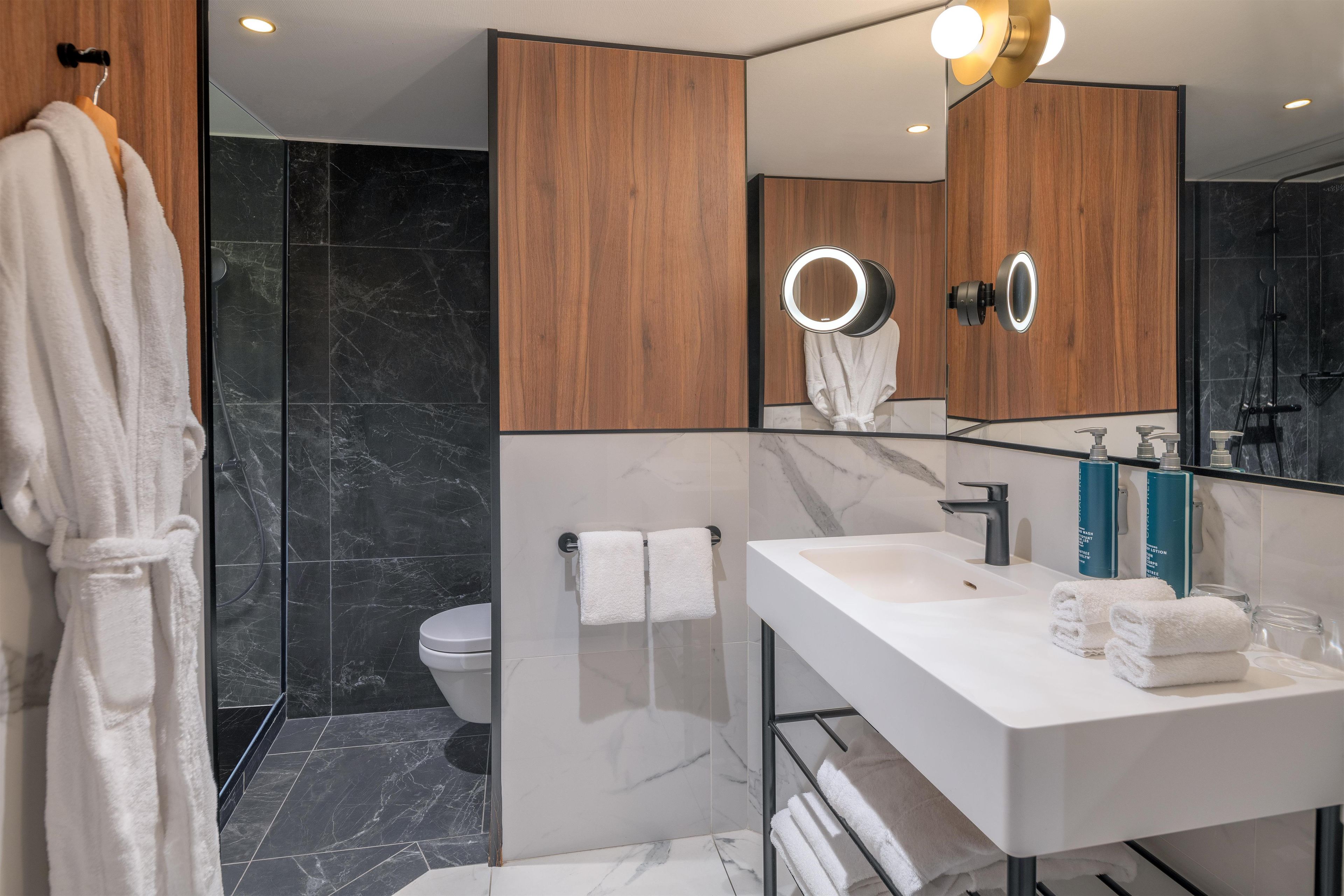A modern bathroom with a large mirror, a white sink, and a shower.