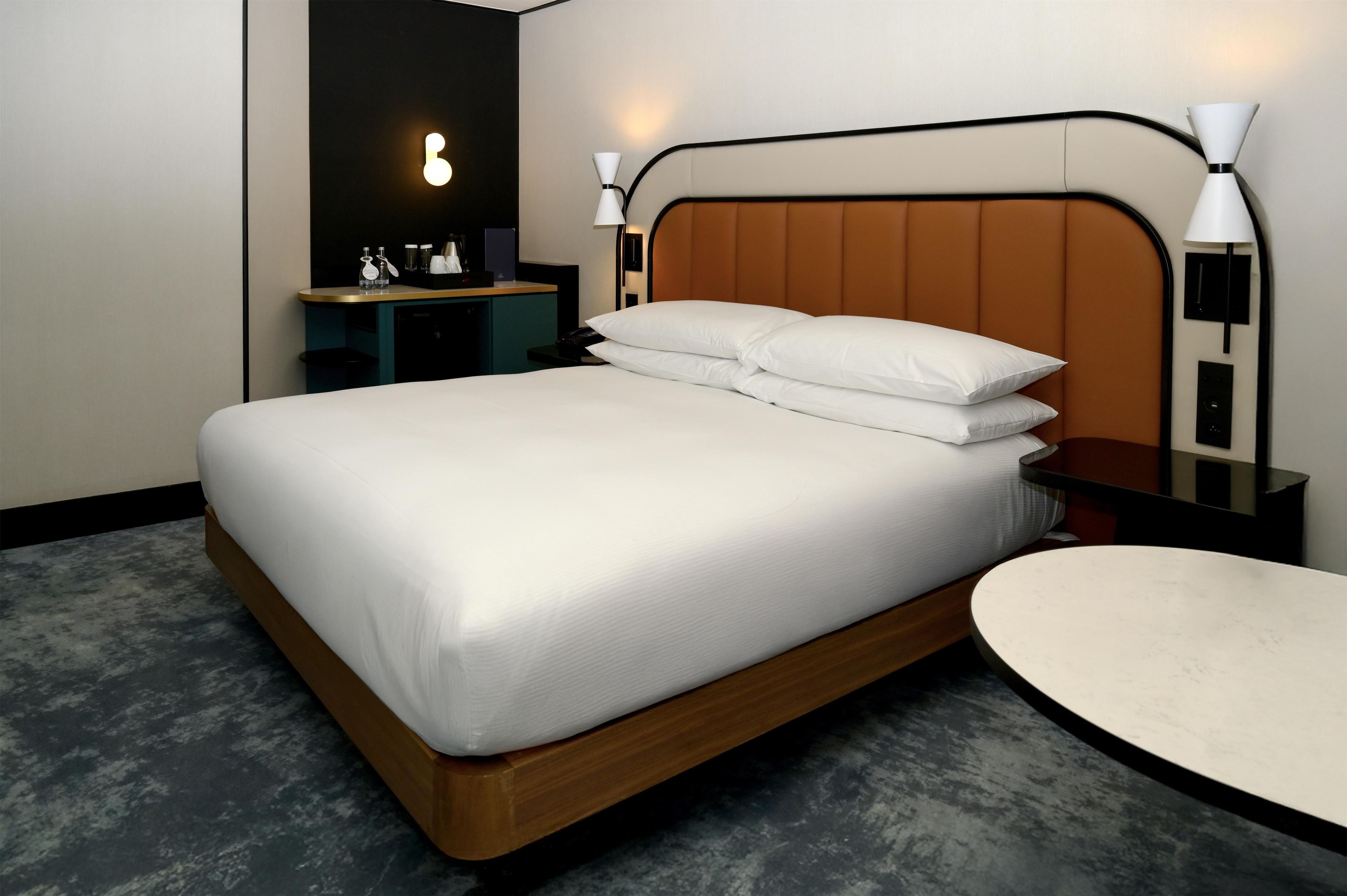 A modern hotel room with a large bed, bedside tables, a small desk, and a round seating area.