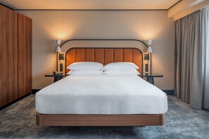 Habitación de hotel con una cama grande, dos mesitas de noche, un cabecero de madera y una mesita con una lámpara.