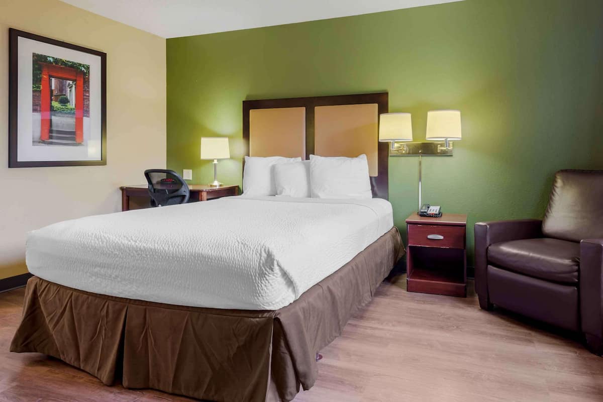 A hotel room with a large bed, two bedside tables with lamps, a chair, and a framed picture on the wall.