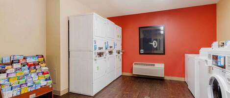 A laundry room with multiple washers and dryers, a wall-mounted air conditioner, and a rack of laundry cards.