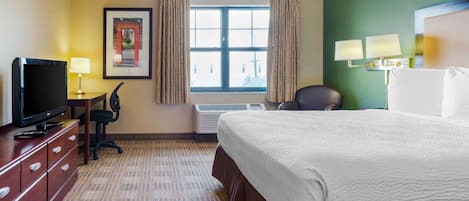 Habitación de hotel con una cama, un escritorio con lámpara, un televisor y un cuadro en la pared.