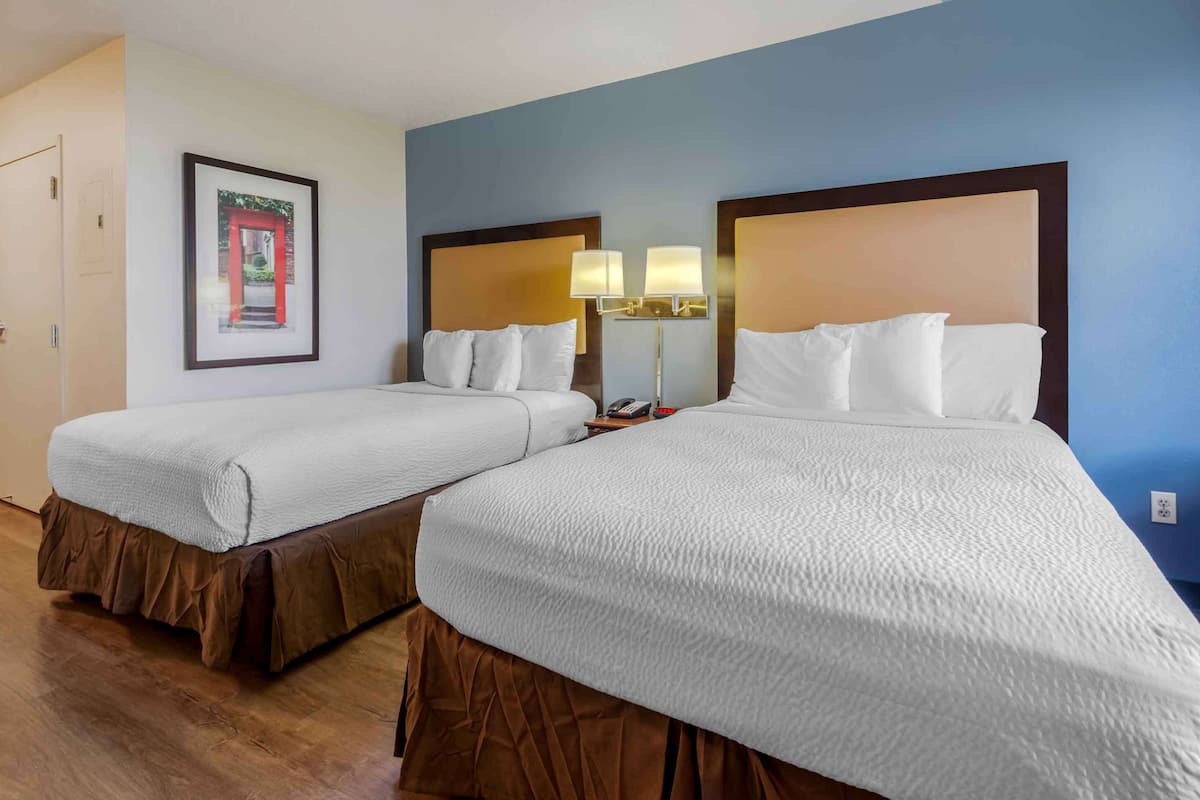 A hotel room with two beds, a framed picture on the wall, and a nightstand with a lamp.