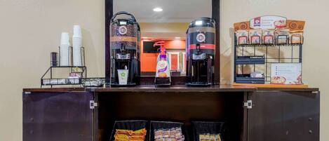 Una estación de café con dos cafeteras, un dispensador de café y una exhibición de tazas y paquetes de café.