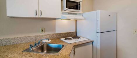 Una cocina con armarios blancos, microondas, refrigerador, fregadero y estufa a gas.