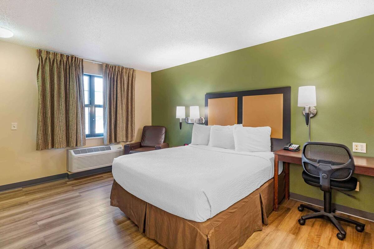 Hotelkamer met een groot bed, een bureau met stoel, een raam met gordijnen en een wandlamp.