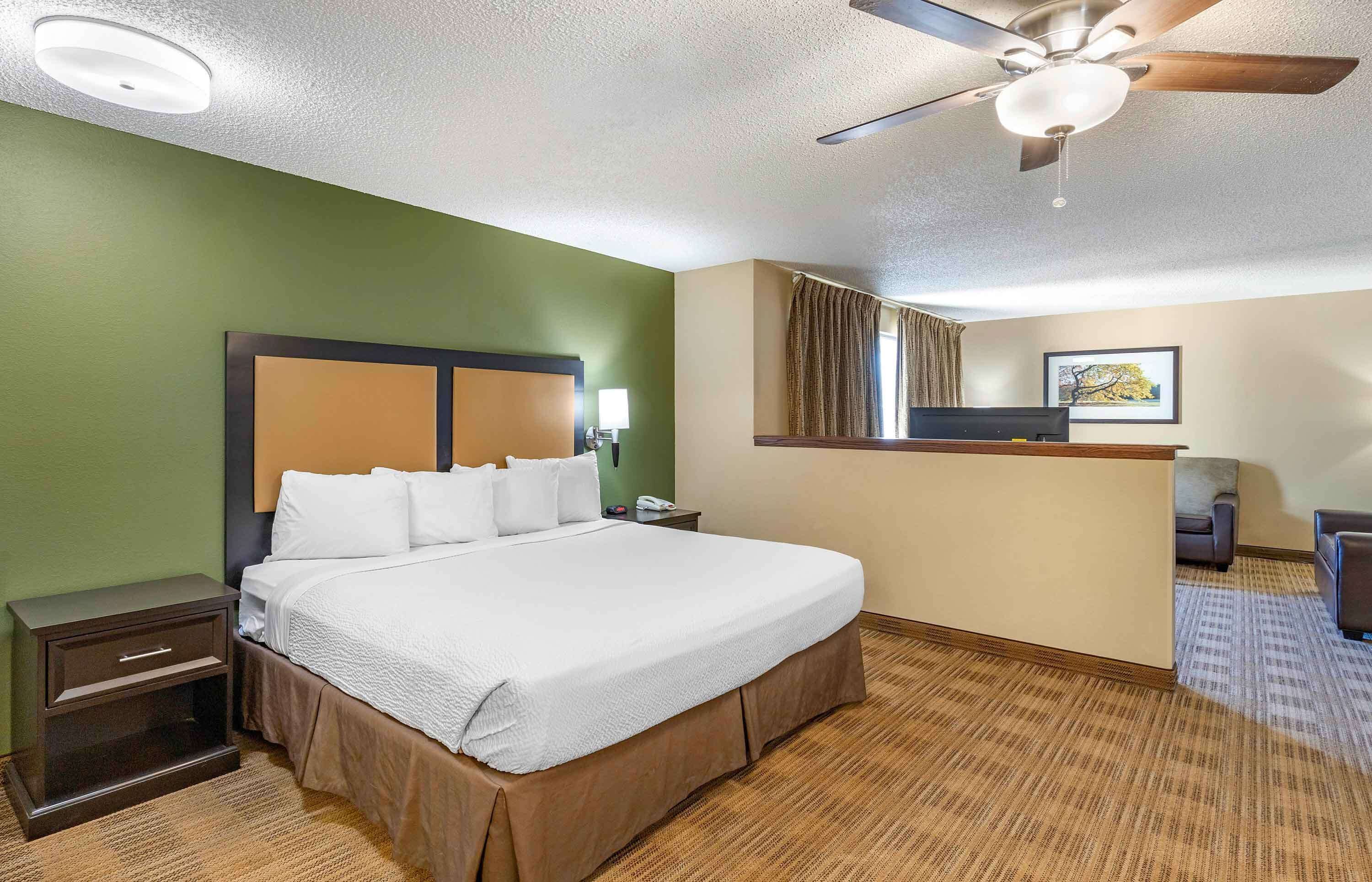 Habitación de hotel con una cama grande, un escritorio, una silla, un ventilador de techo y una ventana con cortinas.