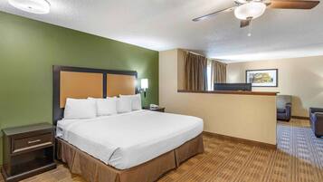 Habitación de hotel con una cama grande, un escritorio, una silla, un ventilador de techo y una ventana con cortinas.