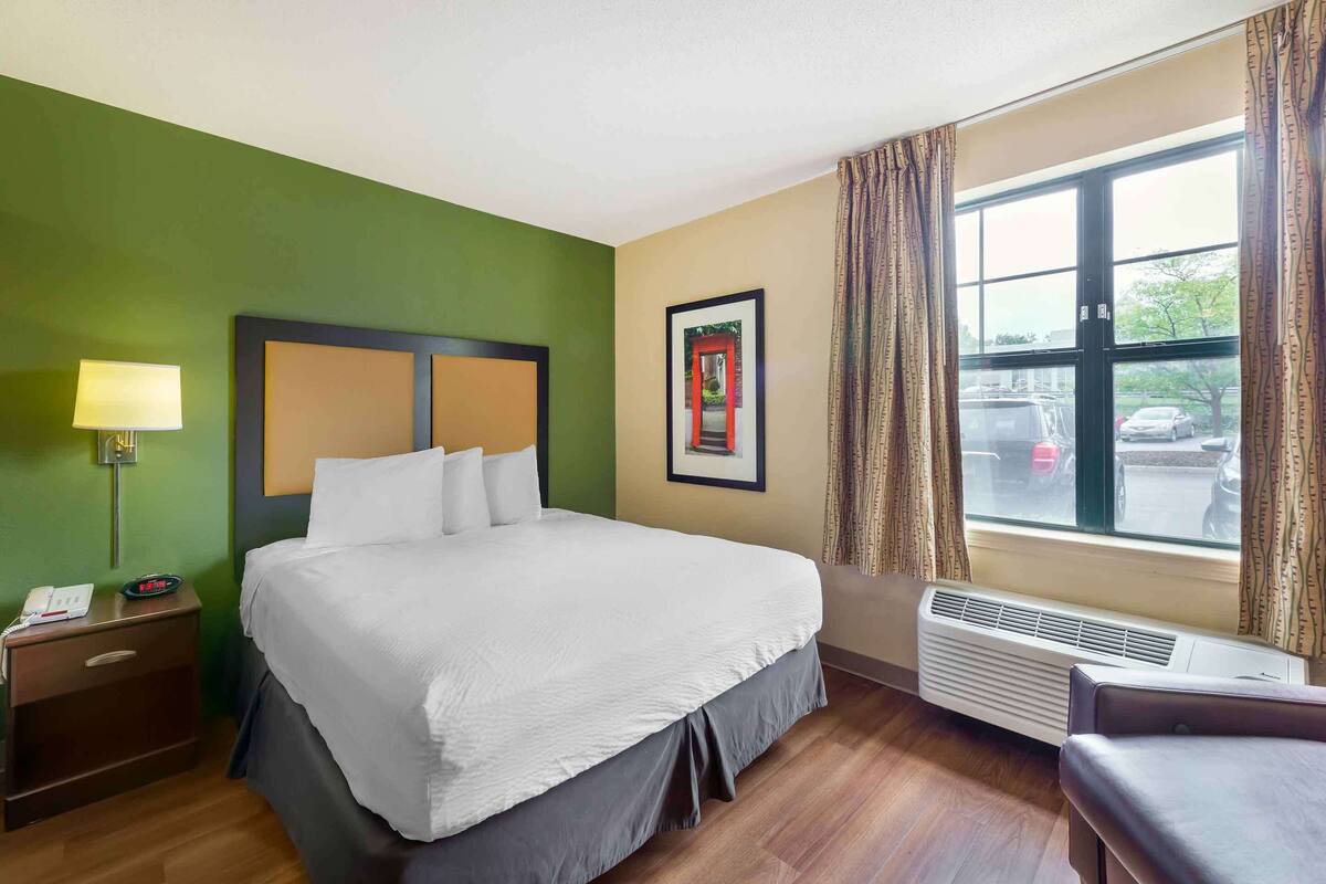 Hotelkamer met een bed, nachtkastje, lamp, airconditioning en een raam met gordijnen.