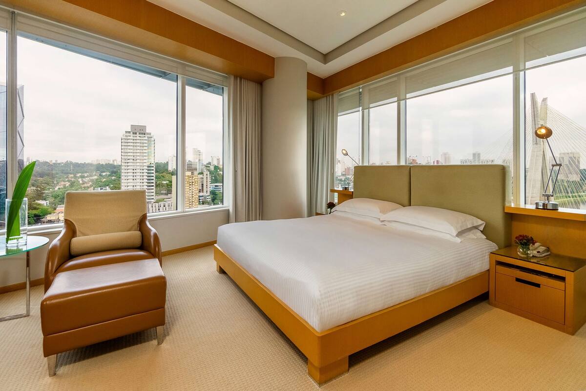 Una habitación de hotel moderna con una cama grande, una zona de estar y vistas a la ciudad.