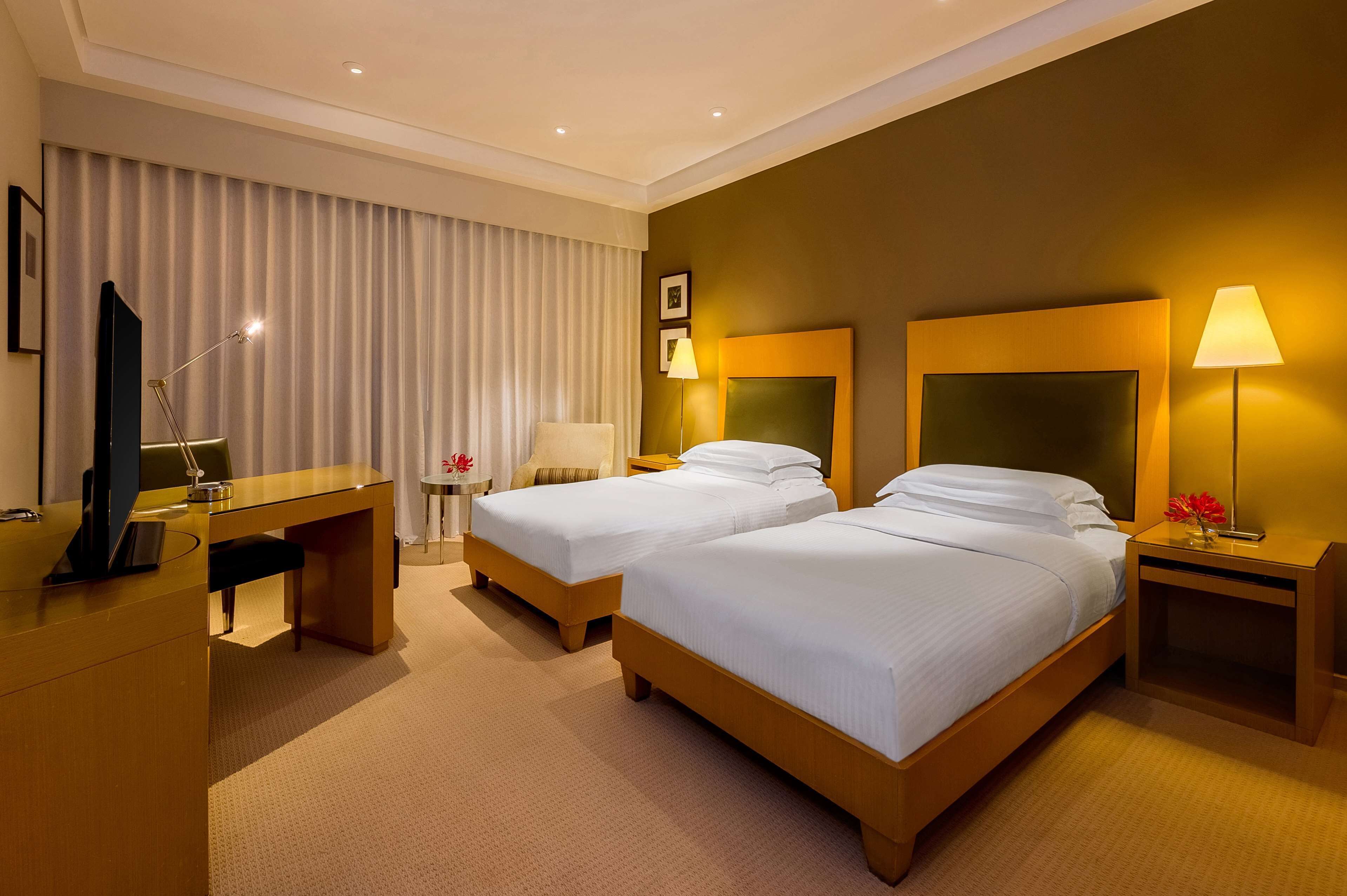A hotel room with two beds, a desk, a chair, and a TV.