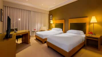 A hotel room with two beds, a desk, a chair, and a TV.
